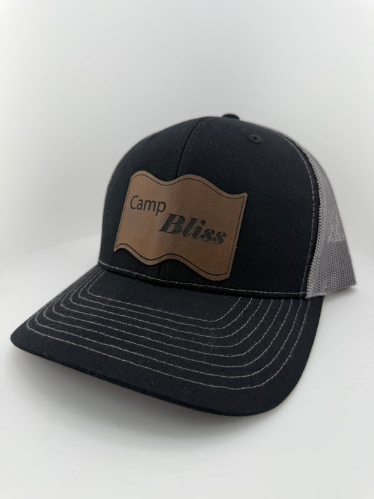 Baseball hat with Camp Bliss logo in leatherette on the front. Front of hat is black and back of hat is grey mesh