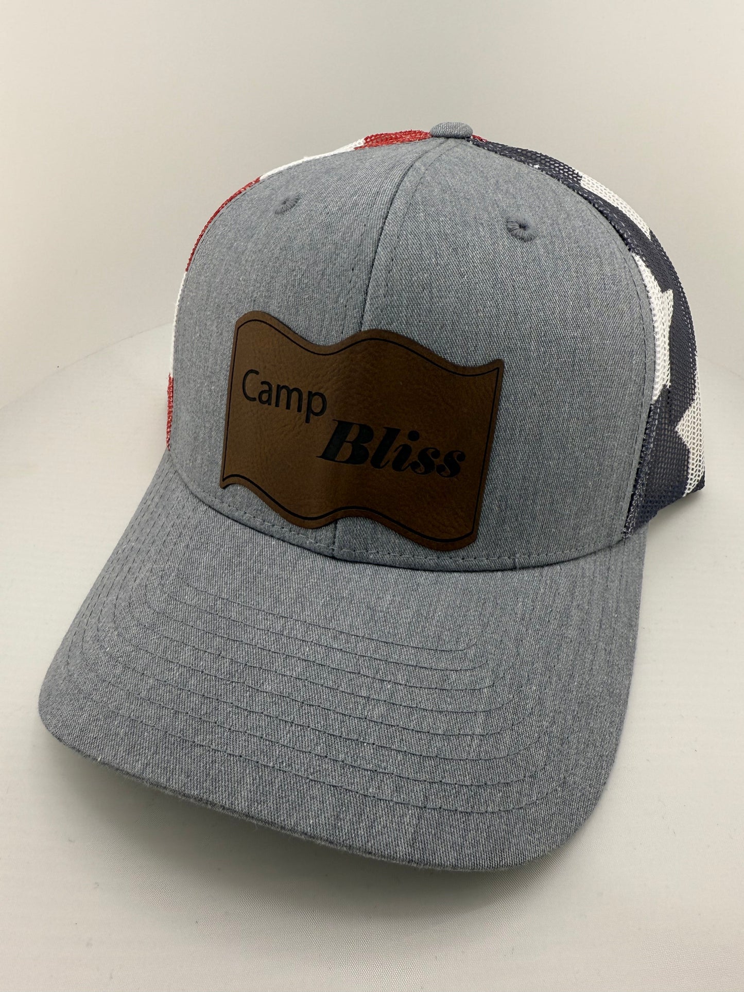 Baseball hat with Camp Bliss logo in leatherette on the front. Front of hat is grey and back of hat is american flag mesh. 