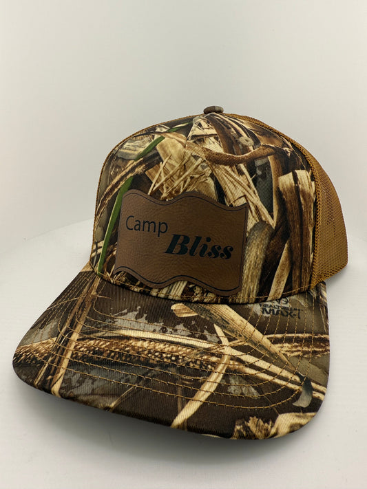Baseball hat with Camp Bliss logo in leatherette on the front. Front of hat is realtree camo and back of hat is Brown mesh